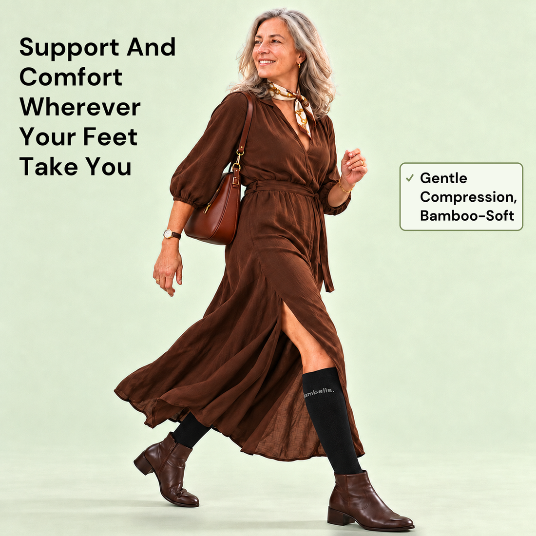 A woman in her fifties with silver hair walks briskly in a brown midi dress and ankle boots, a shoulder bag on her arm, wearing black knee-high Bambelle StepMassage Arch Socks. Text: Support And Comfort Wherever Your Feet Take You. Gentle Compression, Bamboo-Soft