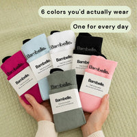 The six Bambelle StepMassage Arch Socks colors held in two hands: dark pink, light blue, white, black, light pink and gray, each with its Bambelle. bellyband